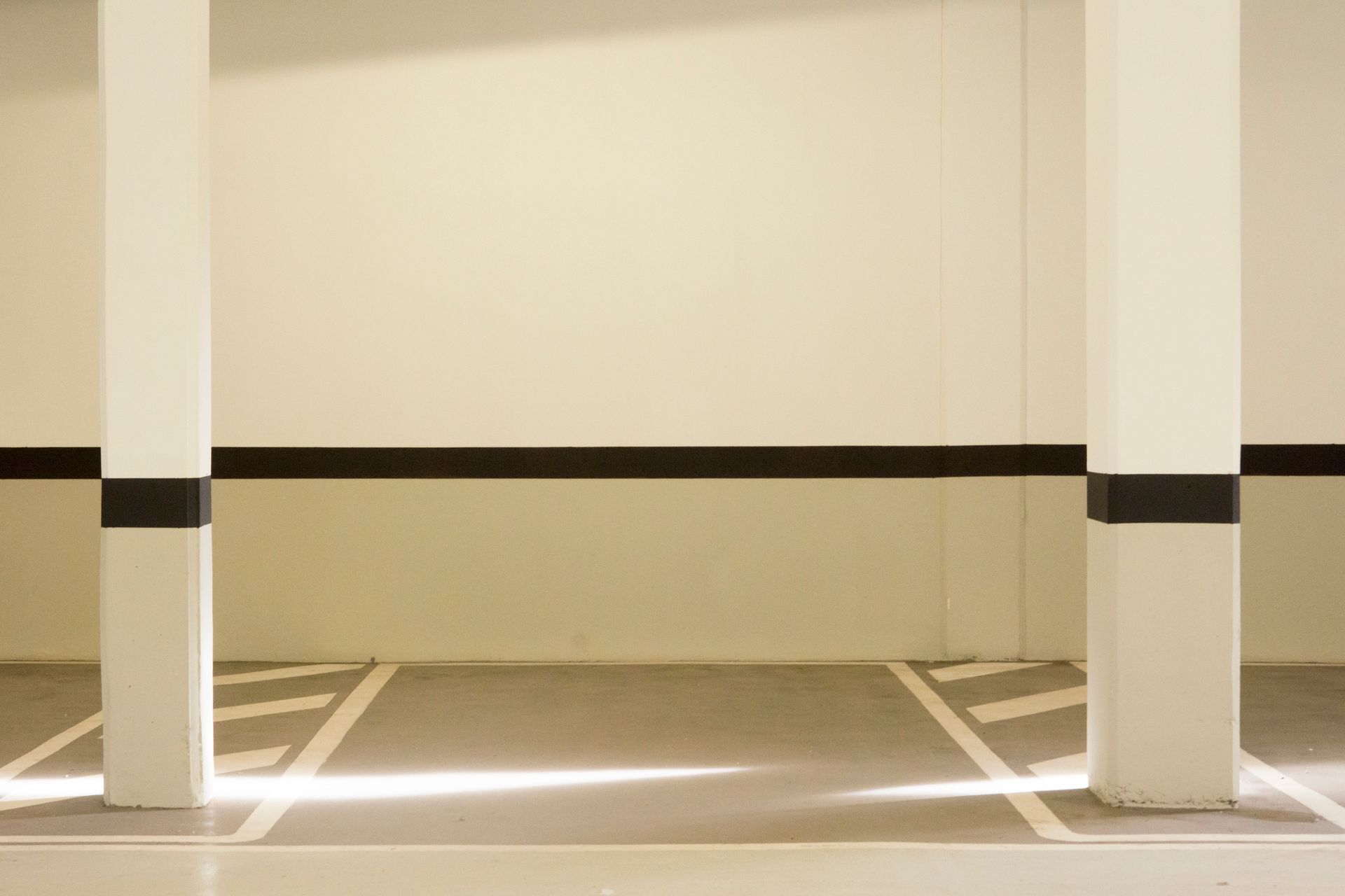 A minimalist view of a well-lit, empty parking garage interior featuring structural posts.