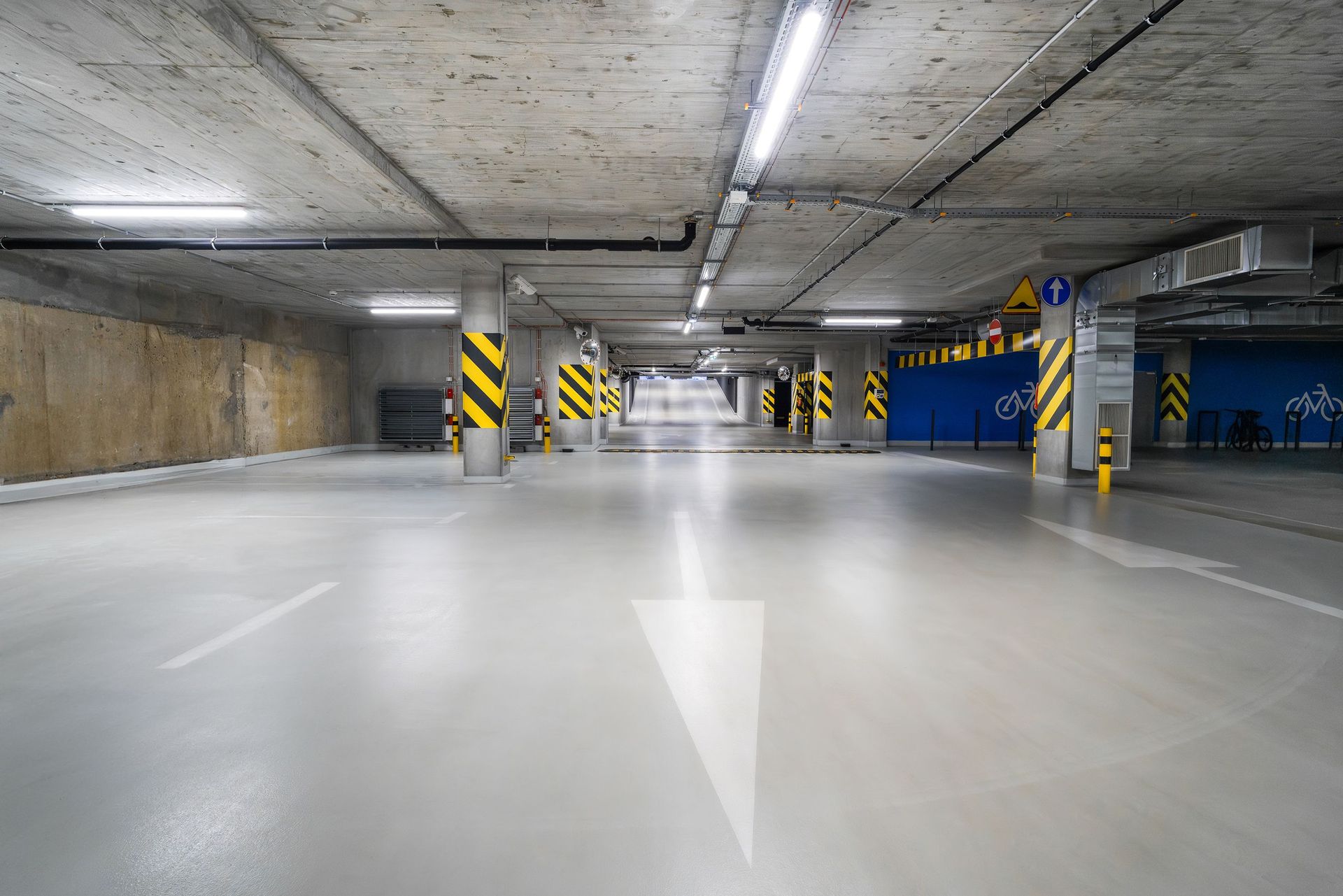 Explore the modern, well-lit, and spacious underground parking garage in Poznań with clear directional signs.
