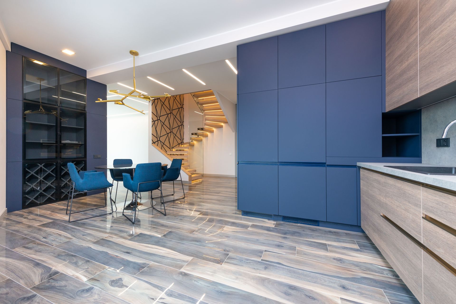 Contemporary kitchen with cabinets and table with armchairs against staircase on floor in light house
